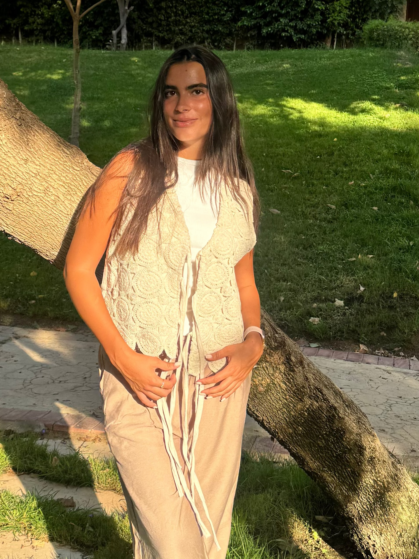 Person standing next to a large tree in a park-like setting with green grass and trees.