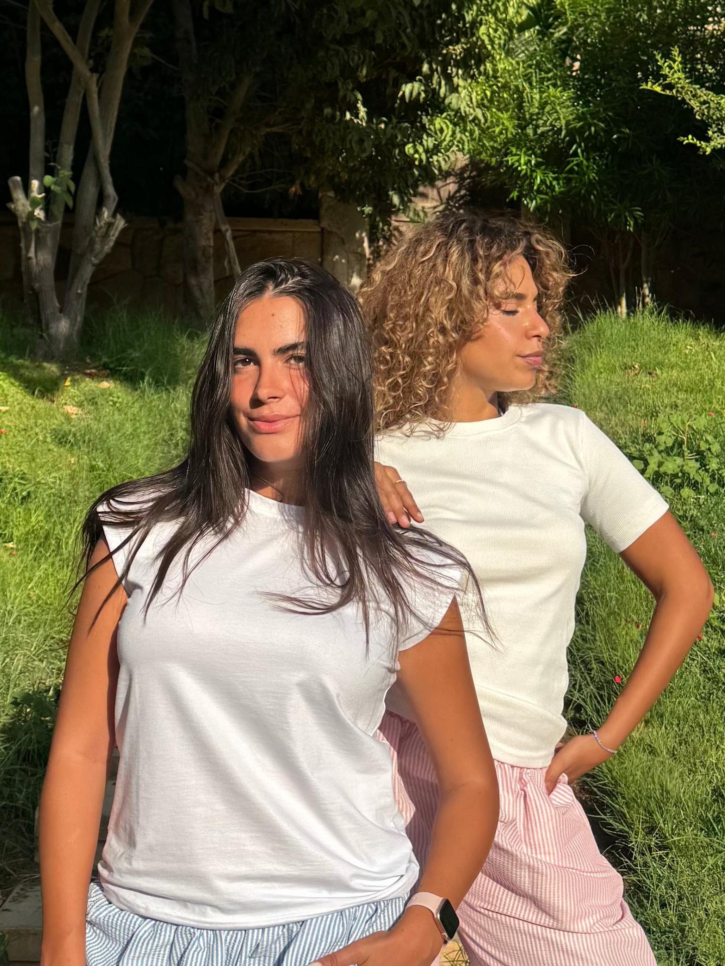 Two people standing outdoors on a grassy area with trees in the background
