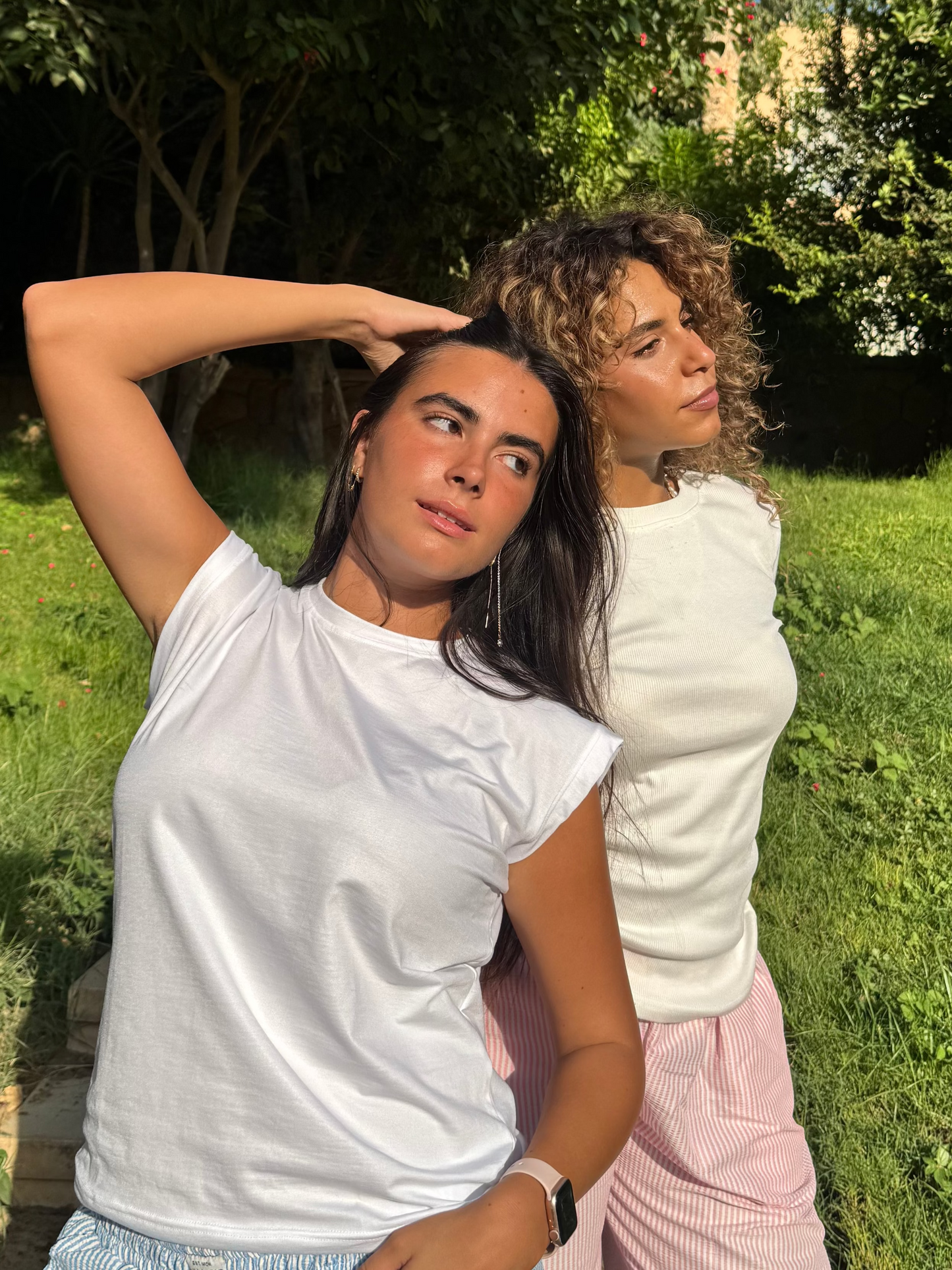 Two women standing in a grassy area with trees and a clear sky.