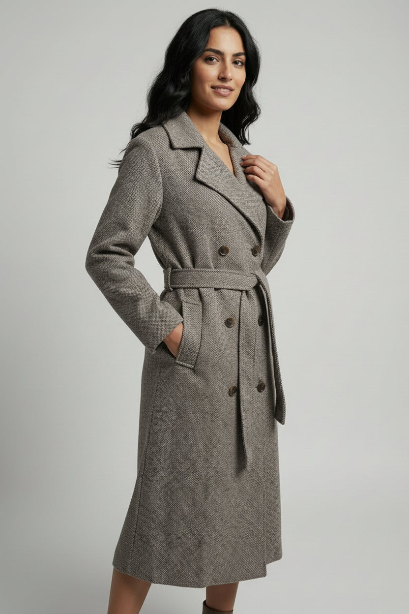 Woman wearing a gray coat with a belt on a plain background