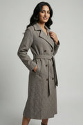 Woman wearing a gray coat with a belt on a plain background