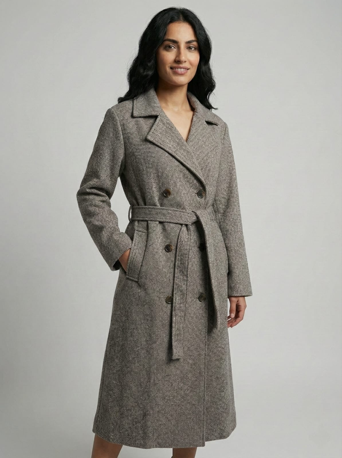 Woman wearing a gray coat with a belt on a plain background