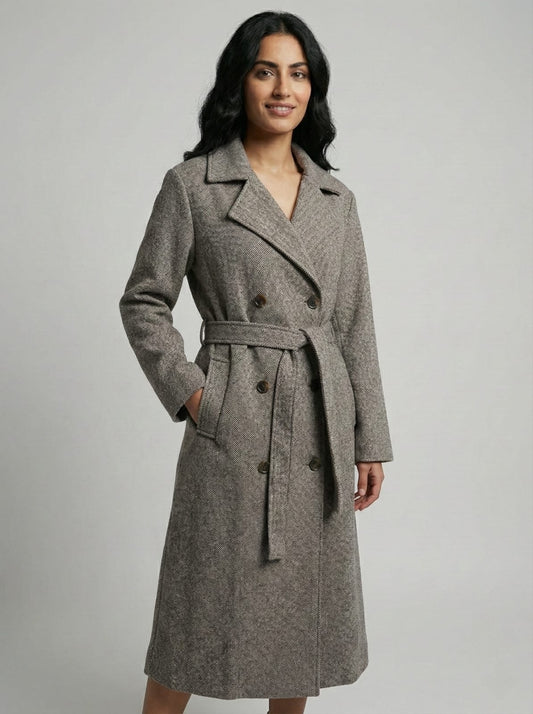 Woman wearing a gray coat with a belt on a plain background