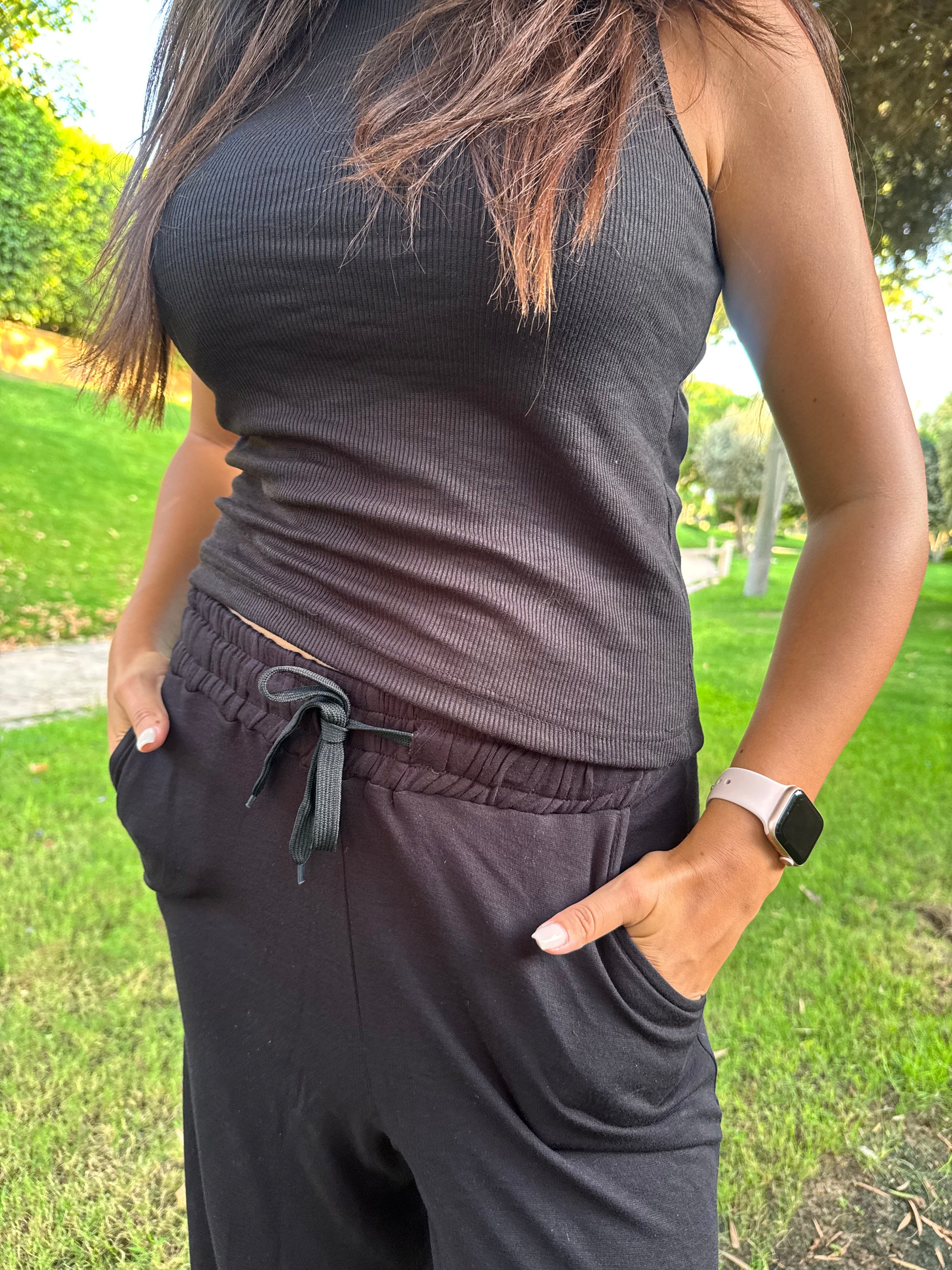 Person wearing a dark sleeveless top and pants outdoors on a grassy area.
