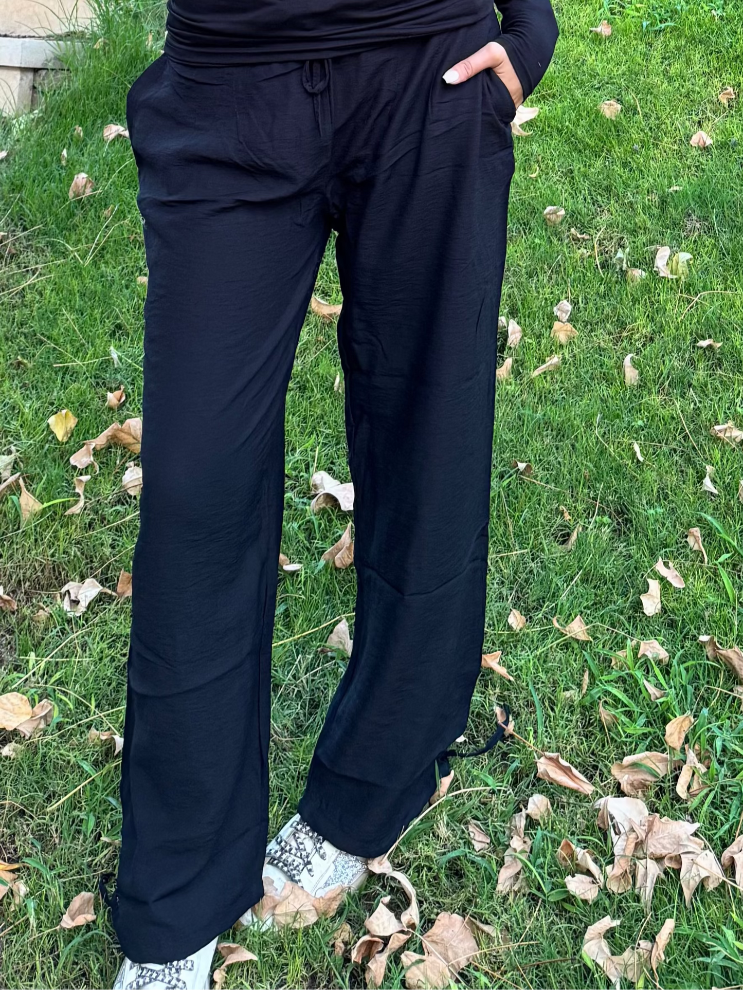 Woman in black outfit standing next to a tree in a garden