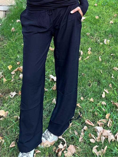 Woman in black outfit standing next to a tree in a garden
