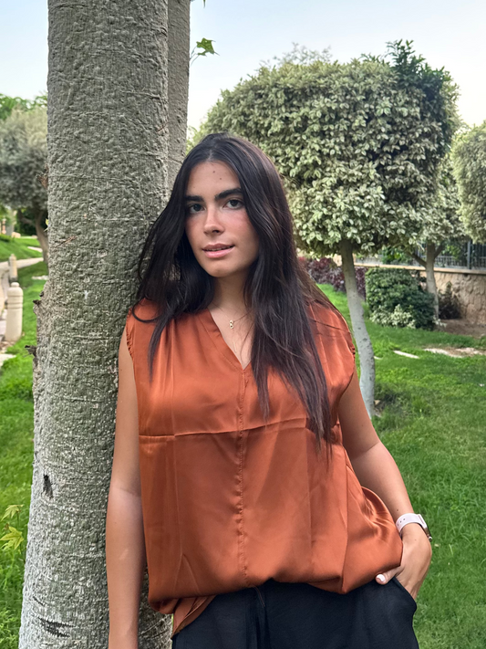 Woman in an orange top standing next to a tree in a park